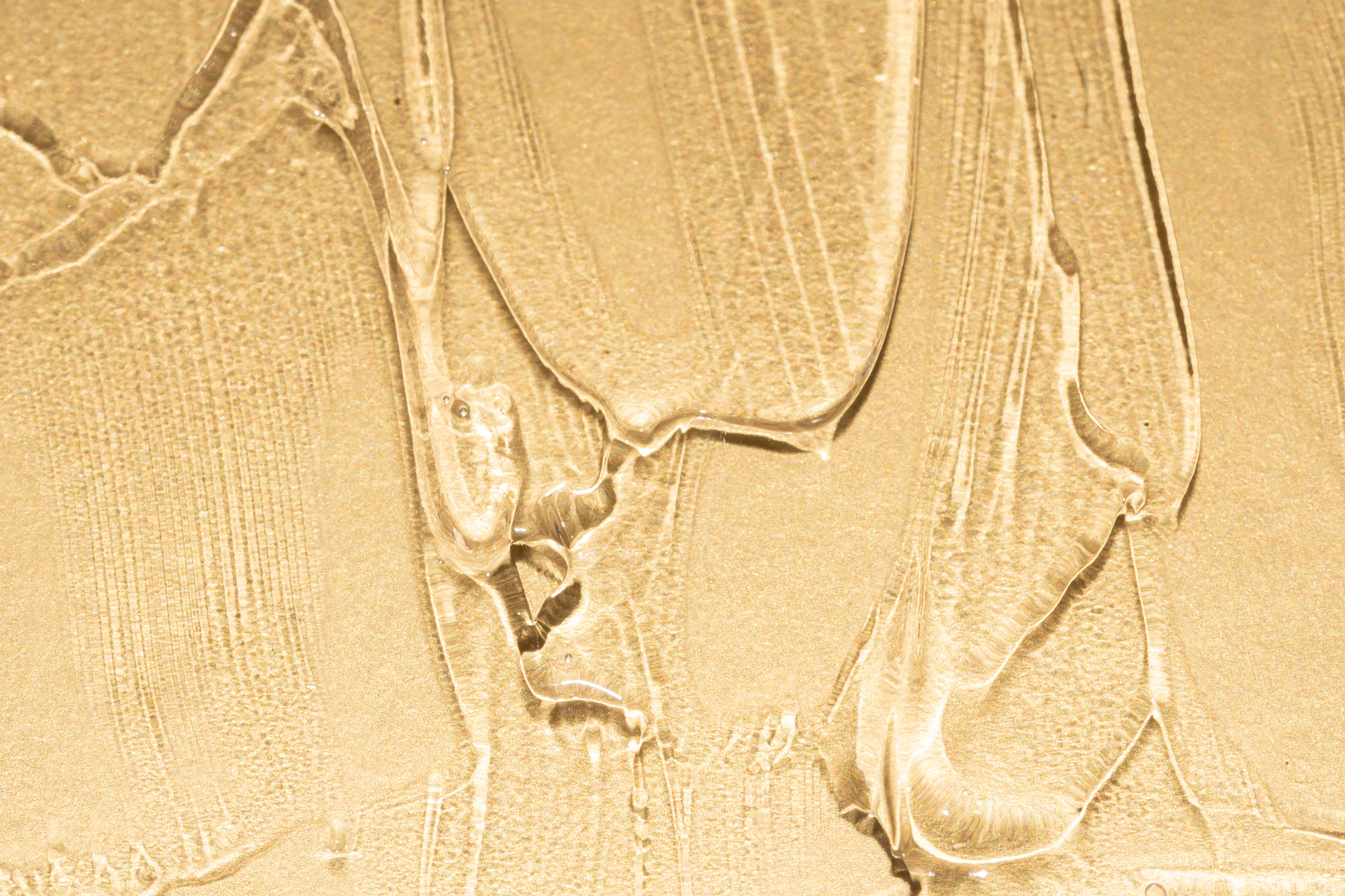 Close-up of a translucent gel-like firming serum with a dewy texture on a luxurious gold background.