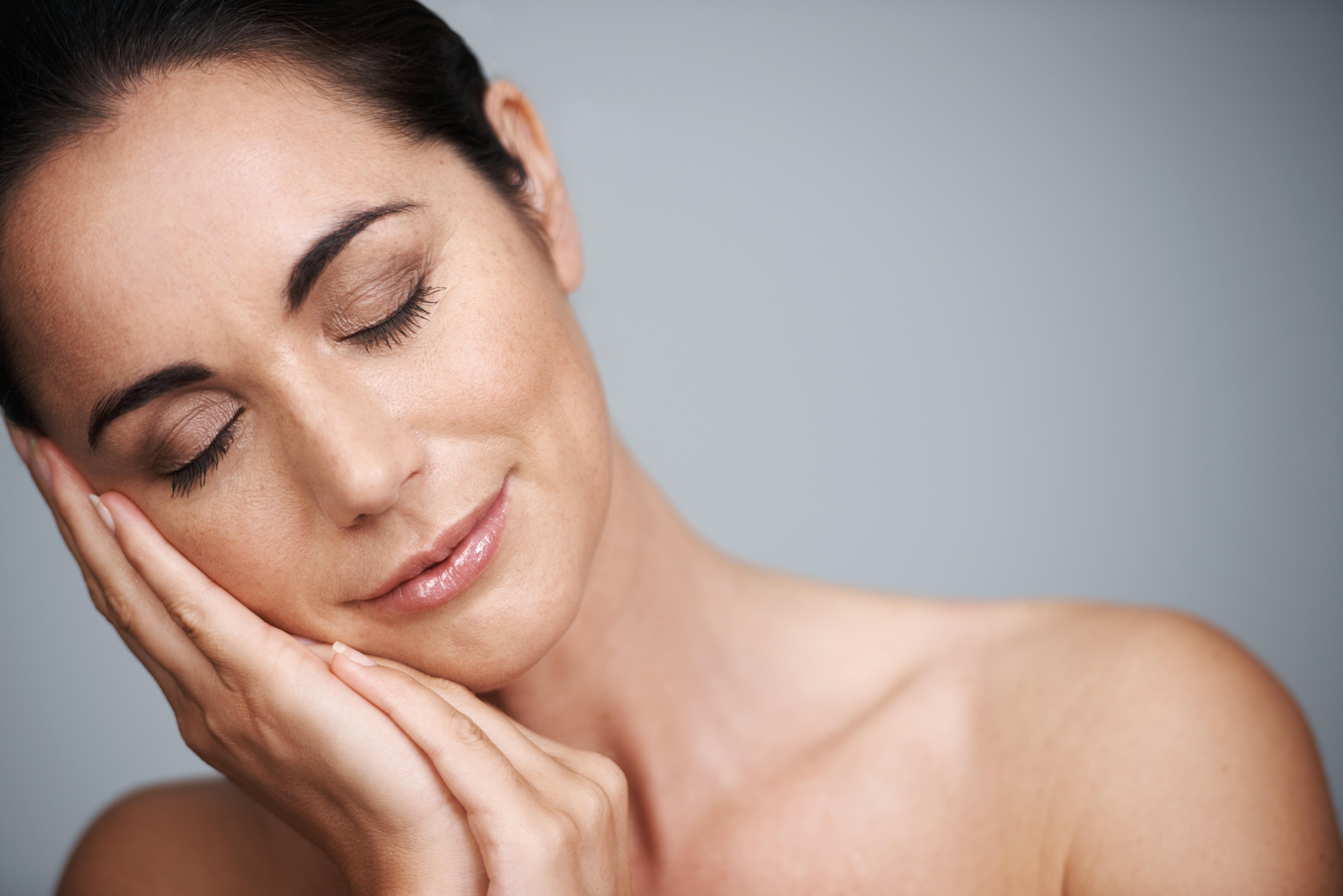 A beautiful, mature woman with healthy, radiant skin is cradling her head in the palms of her hands, seemingly feeling content.