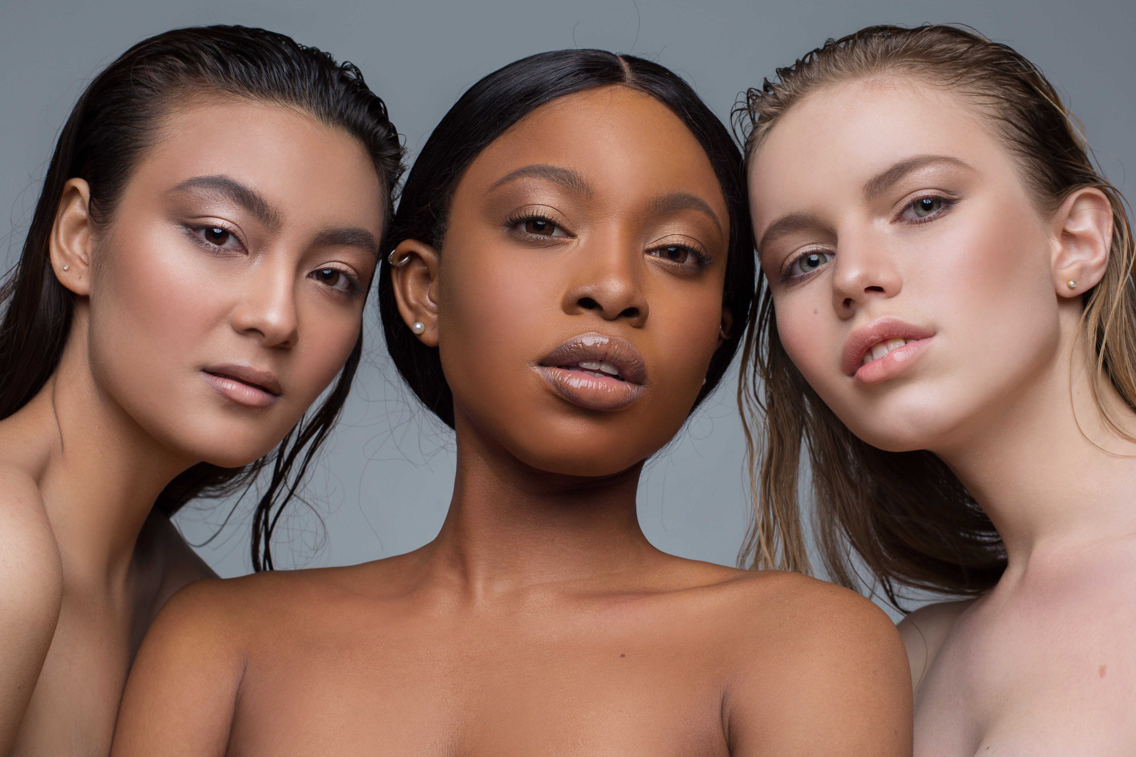 Three young women of different ethnicity-Asian, black and white-posing together for a picture in a model-like setting, beautiful and serious looking.
